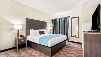 Habitación de hotel con cama, mesita de noche, lámpara y espejo.