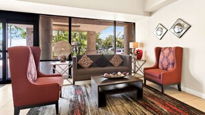 Un salon moderne comprenant un canapé, deux fauteuils, une table basse et une grande fenêtre donnant sur des palmiers.