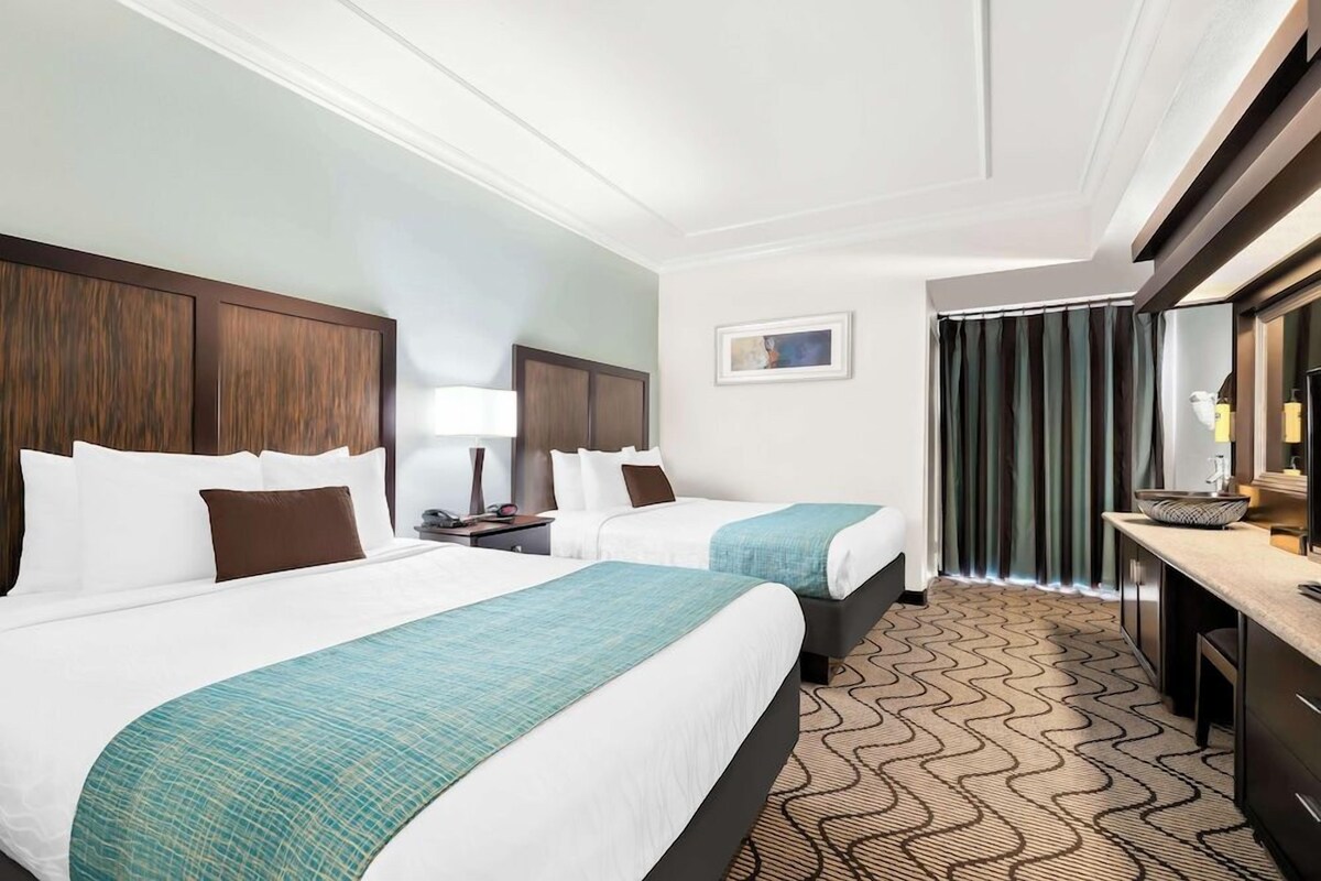 A hotel room with two beds, a desk, a mirror, and a patterned carpet.