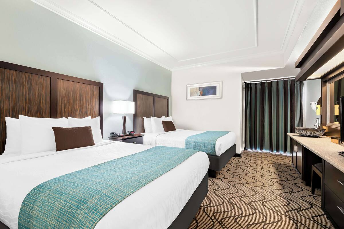 A hotel room with two beds, a desk, a mirror, and a patterned carpet.