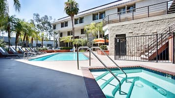 A pool area with two pools, lounge chairs, and a staircase leading to an upper level.
