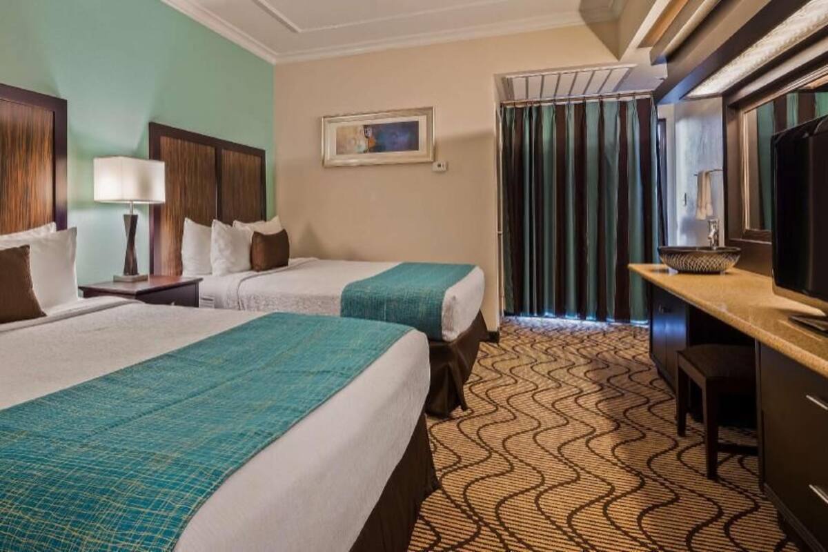 A hotel room with two beds, a desk, a television, and a window with curtains.