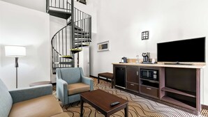 Une chambre d’hôtel moderne dotée d’un escalier en colimaçon, d’un téléviseur à écran plat, d’un canapé, d’une machine à café et d’un four à micro-ondes.