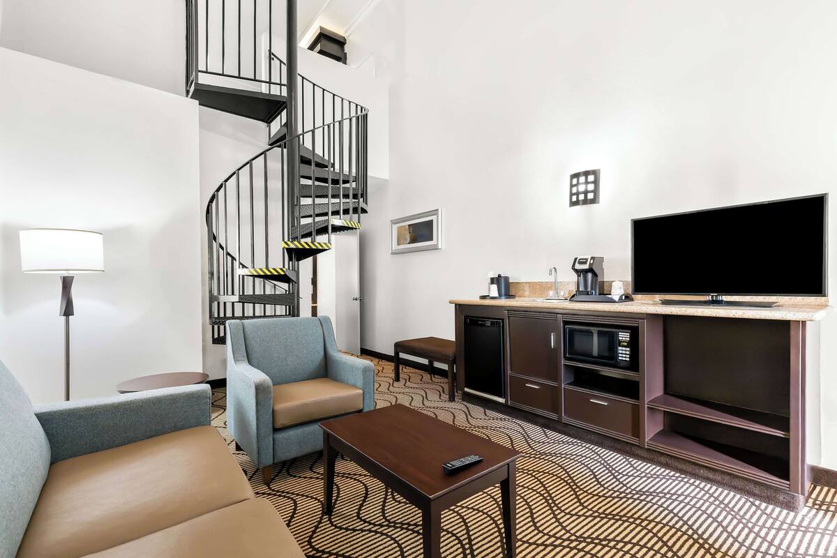 A modern hotel room with a spiral staircase, a flat-screen TV, a sofa, a coffee machine, and a microwave.