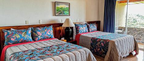 A bedroom with two beds, a wooden ceiling, a painting on the wall, and a view through a window.
