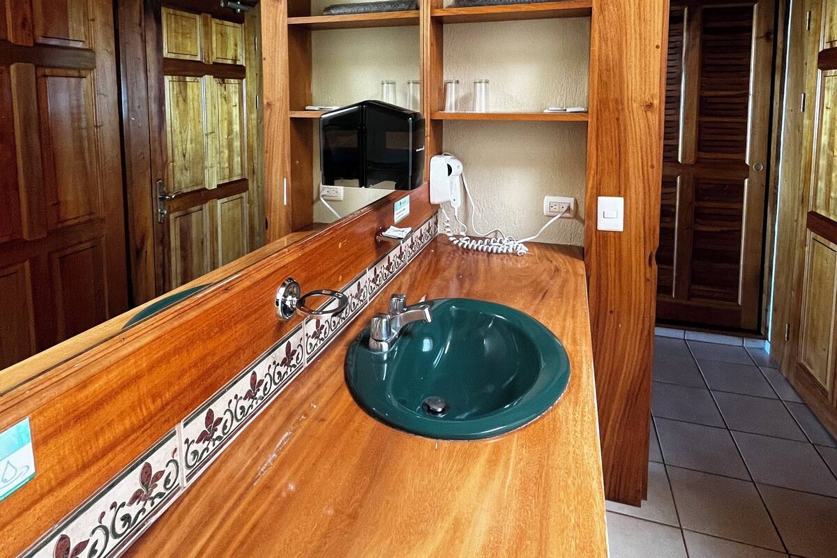 Un baño con tocador de madera, lavamanos verde y espejo.
