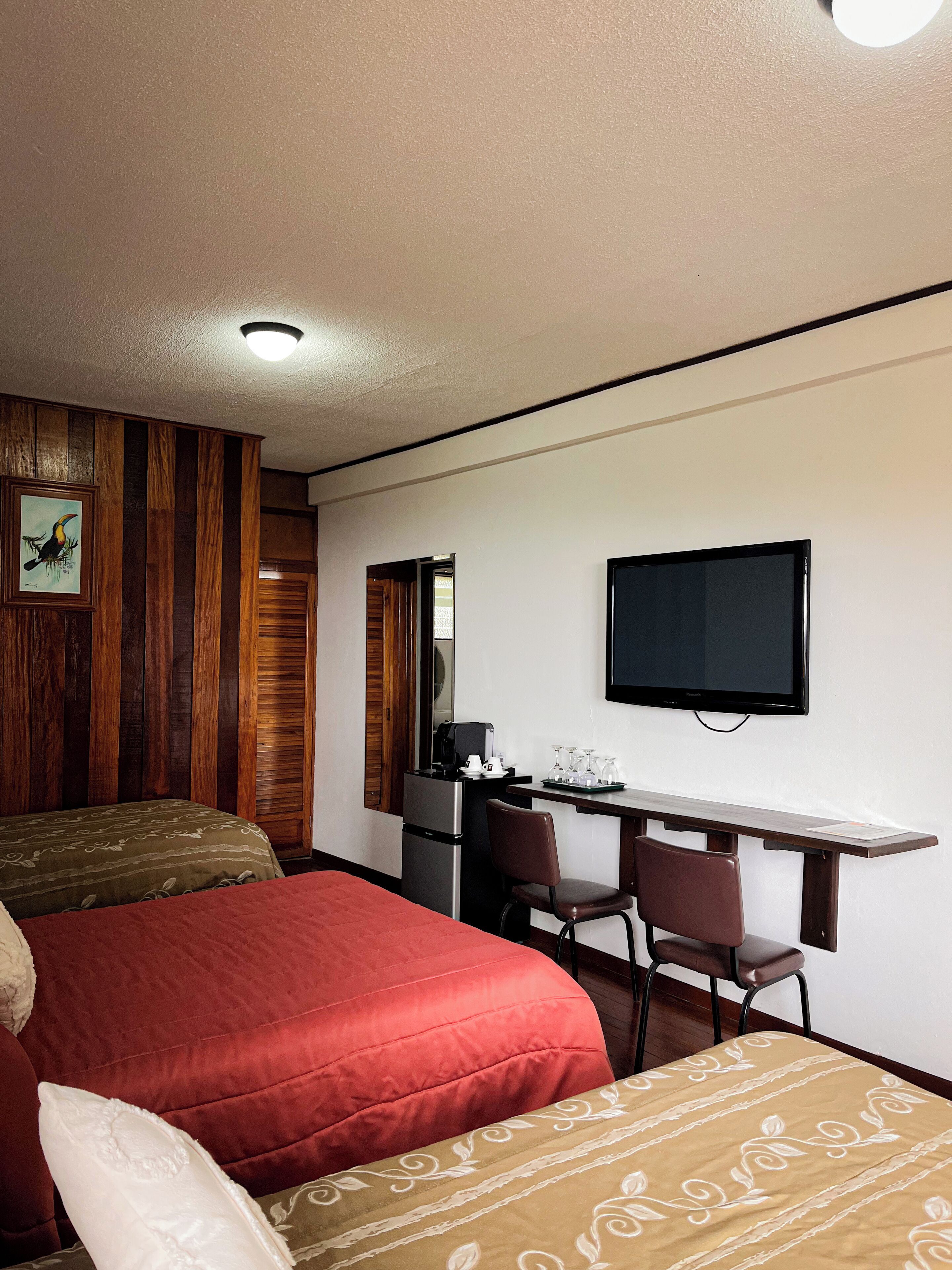 Habitación de hotel con una cama, un escritorio con silla, un televisor y un panel de pared de madera.