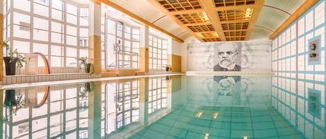 Una piscina interior con agua cristalina, ventanas amplias y un mural en la pared.