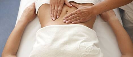 A person receiving a back massage on a massage table in a room with a plain wall and a window.