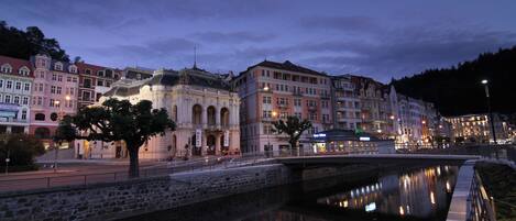 Un edificio histórico con arquitectura clásica, un puente y un río tranquilo que refleja las luces.