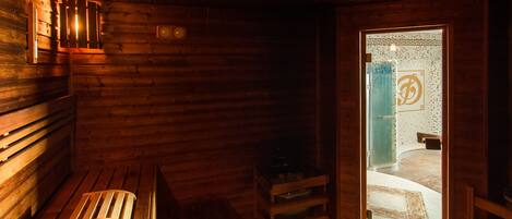 A wooden sauna with benches and a small table, a door leading outside, and a wall-mounted light fixture.