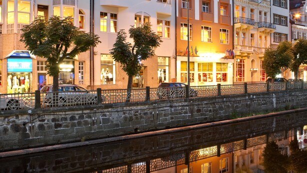 A row of multi-story buildings with balconies, a reflective water body in front, and a sign that reads "HOTEL". - Dvorak Spa & Wellness (Karlovy Vary)