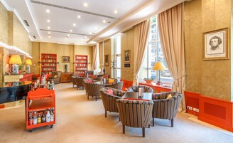 Un vestíbulo de hotel con sillones a rayas, un carrito rojo con botellas y estanterías.