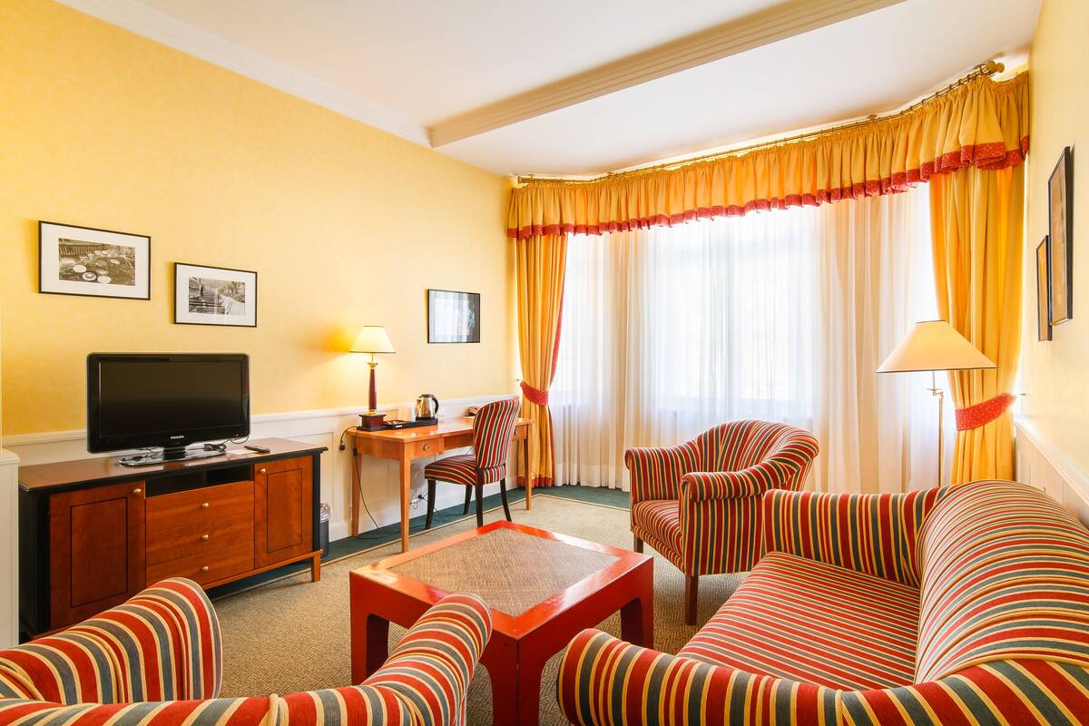 A hotel room with a television, a desk, a chair, a sofa, and a window with curtains.