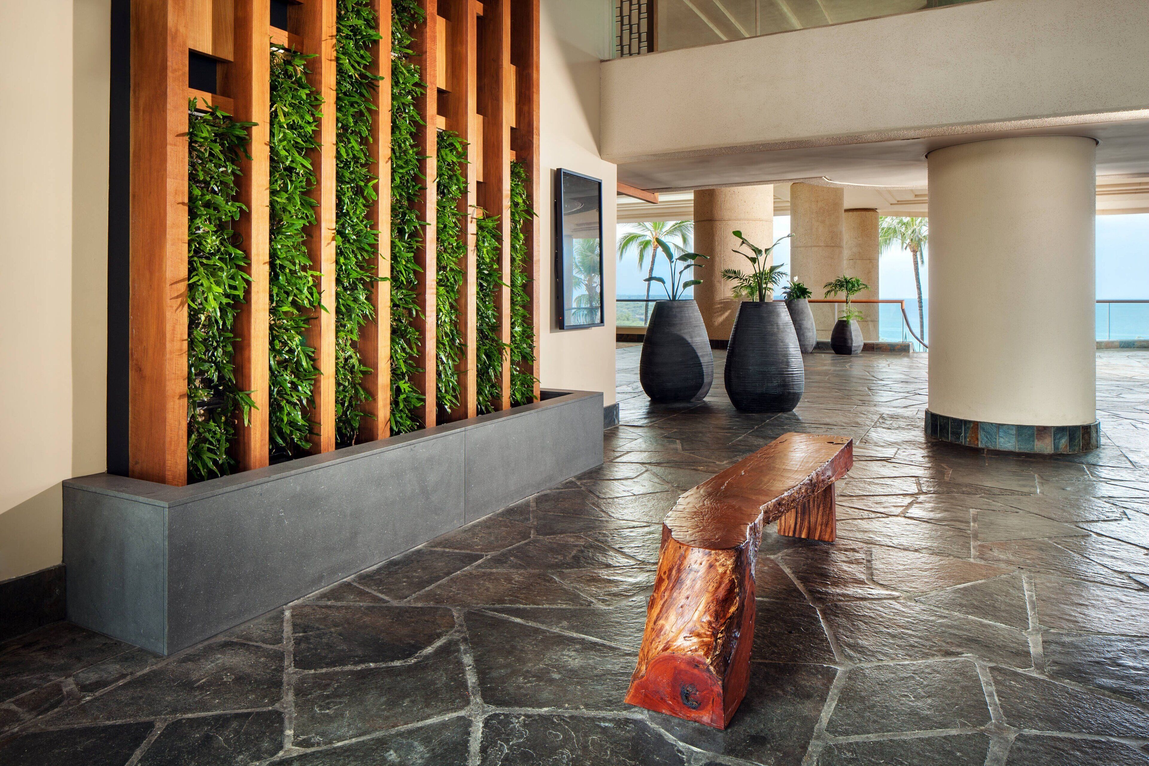 A modern lobby with a stone floor, a wooden bench, vertical garden panels, and large potted plants.
