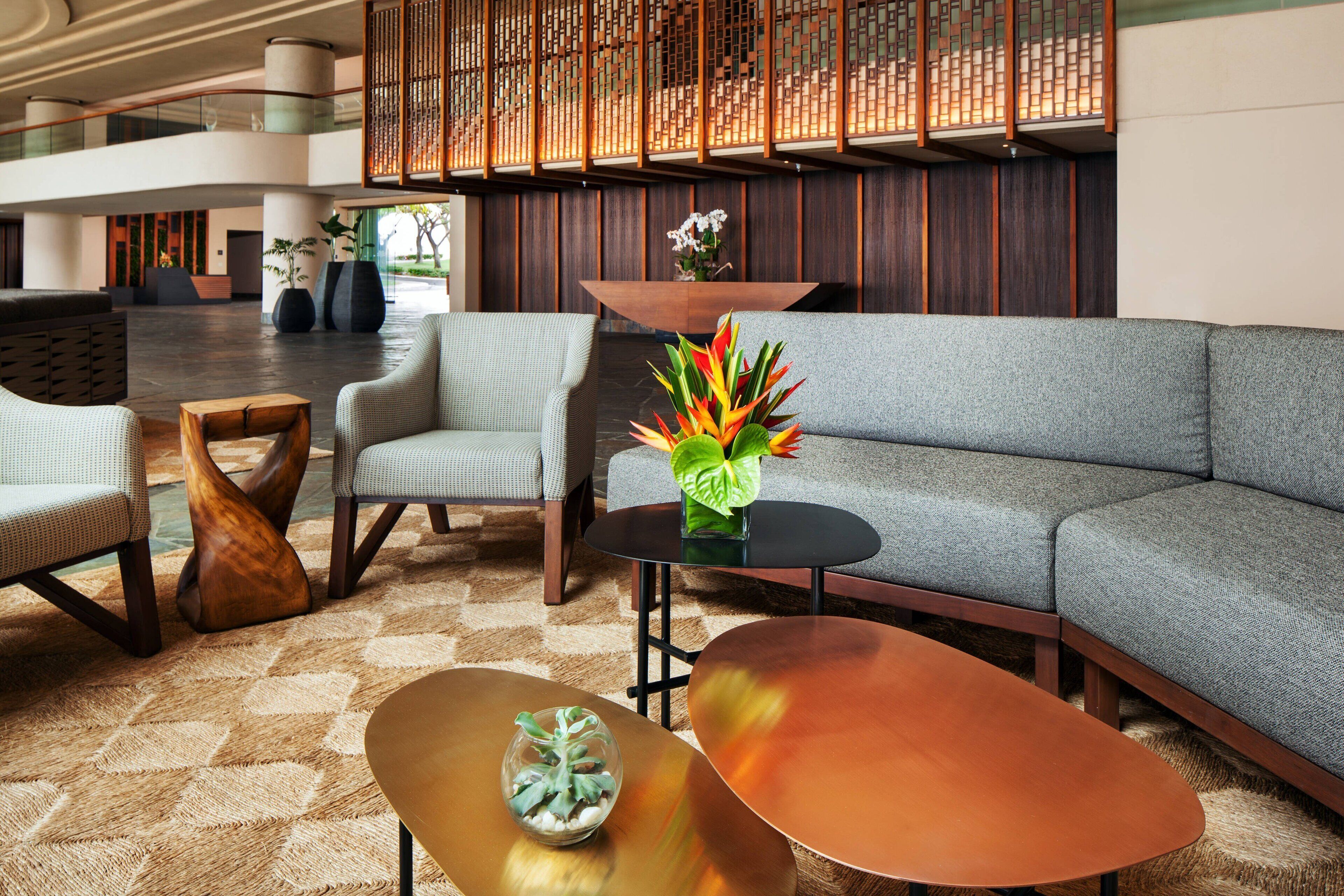 A modern lobby with a grey sectional sofa, a round coffee table, and two armchairs. There is a decorative plant on the coffee table and a wooden sculpture on the floor.
