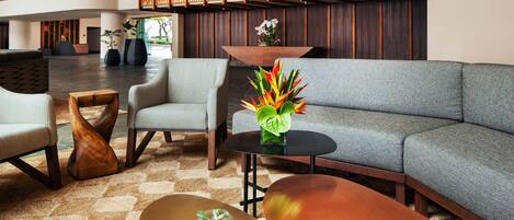A modern lobby with a grey sectional sofa, a round coffee table, and two armchairs. There is a decorative plant on the coffee table and a wooden sculpture on the floor.