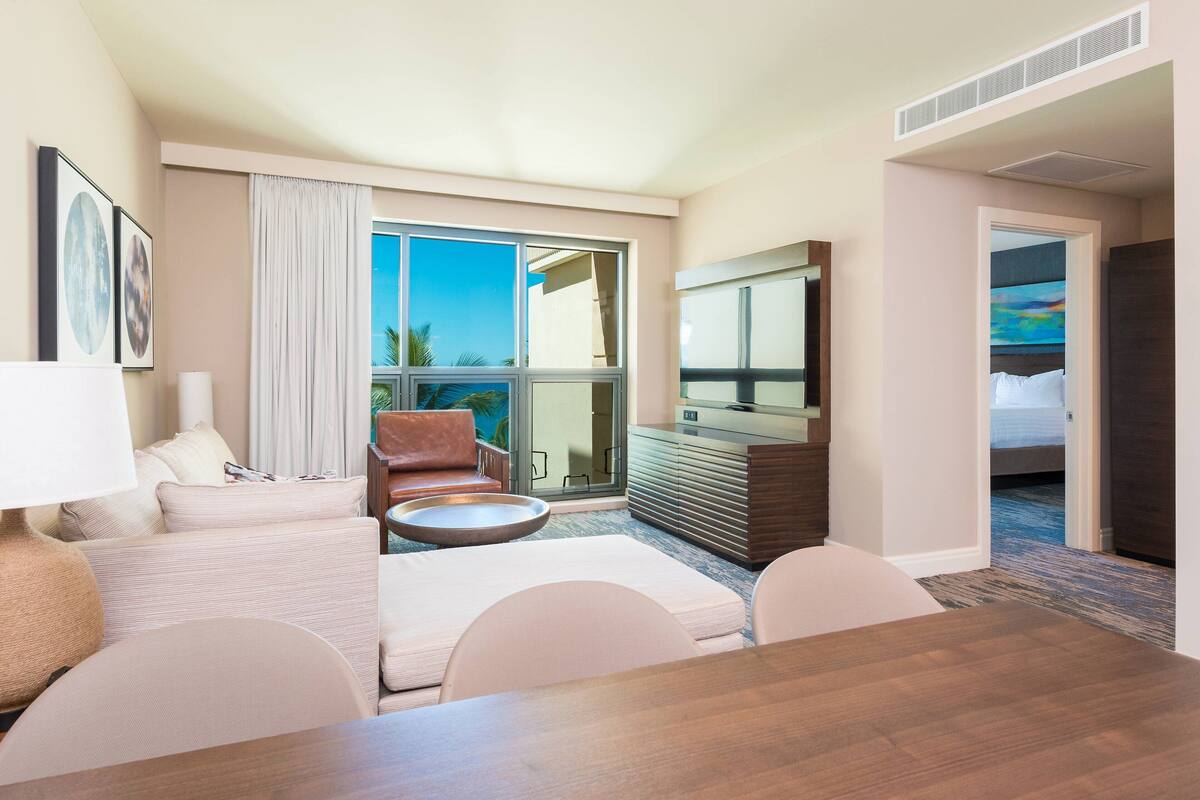 Une chambre d’hôtel avec une grande fenêtre, un canapé, une table à manger, une télévision et un lit.