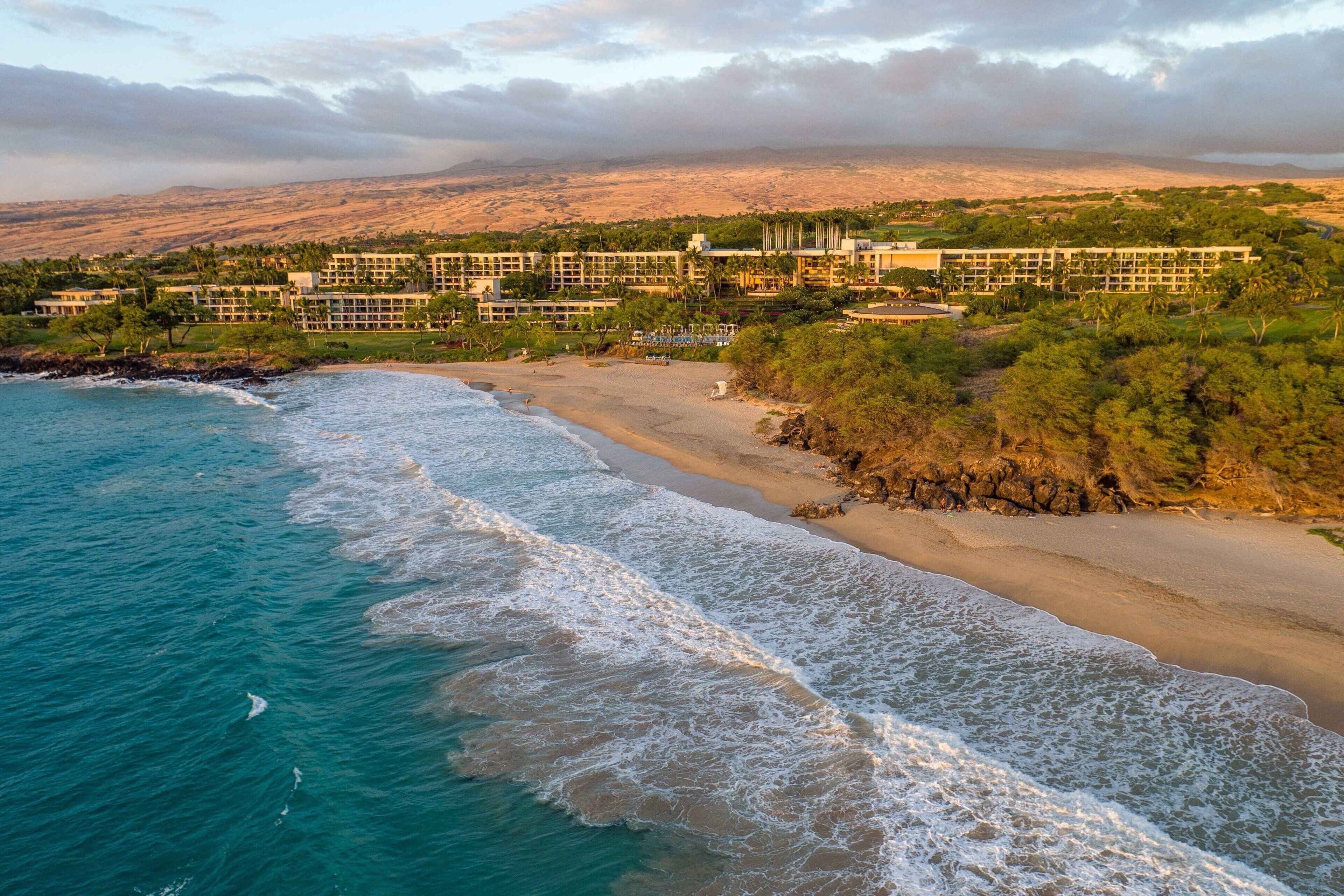 A coastal resort with beachfront properties, a sandy beach, and a mountainous backdrop.