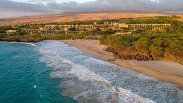 A coastal resort with beachfront properties, a sandy beach, and a mountainous backdrop.
