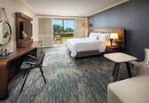A hotel room with a bed, a desk with a chair, a TV, and a lamp.