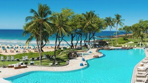 Une piscine de complexe hôtelier bordée de palmiers, agrémentée de parasols de plage et de chaises longues.