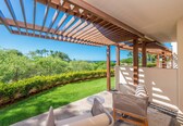 A covered outdoor seating area with a view of a lush garden and the ocean.