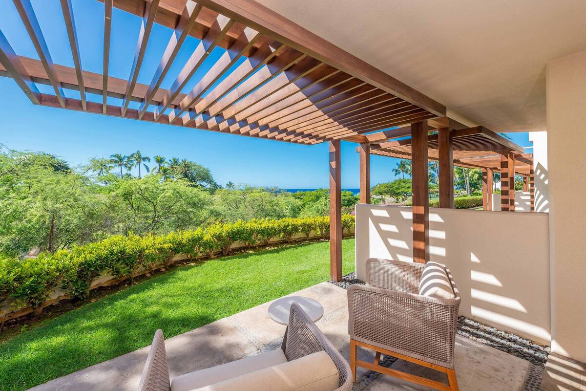 Un espace extérieur abrité, aménagé avec des sièges, et offrant une vue sur un jardin luxuriant et l’océan.