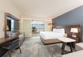 A hotel room with a bed, desk, chair, TV, and a balcony with a view.