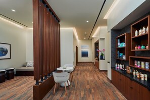 A hallway with a wooden floor, a seating area with a table and chairs, and shelves with various products on the right.