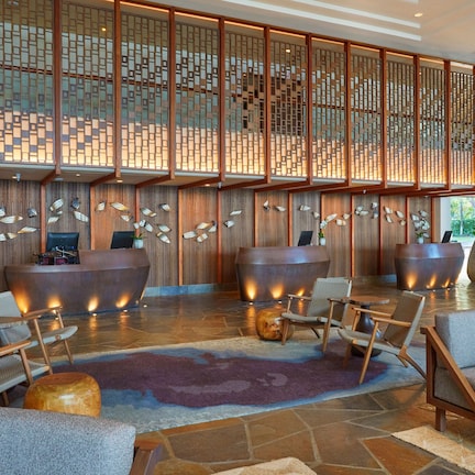 A lobby with a reception desk, seating area, decorative wall panels, and large planters.
