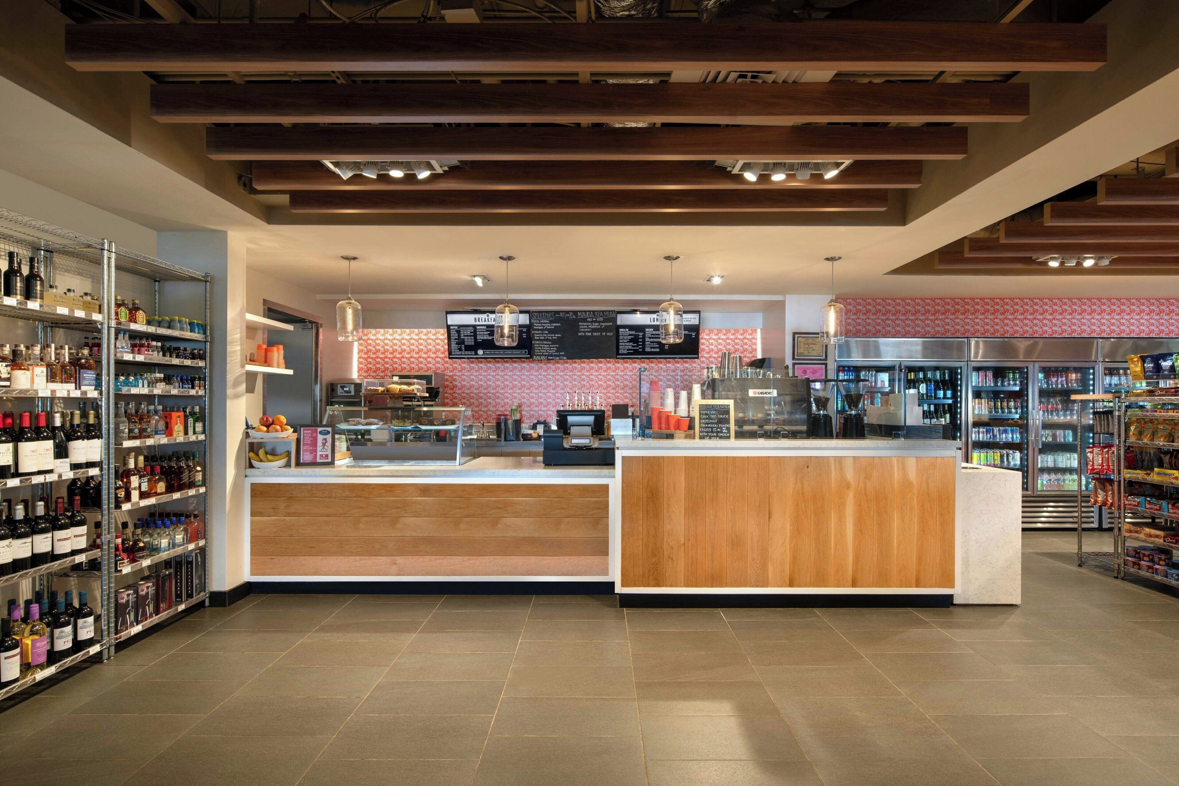 Un espace bar moderne avec un comptoir en bois, des étagères remplies de bouteilles et un tableau affichant le menu.