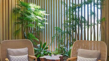 A room with two wicker chairs, a wooden coffee table, and tall plants against a striped wall.