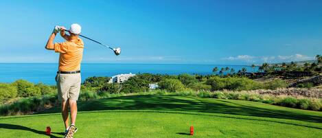 A golf course with a clear view of the ocean and a building in the background.