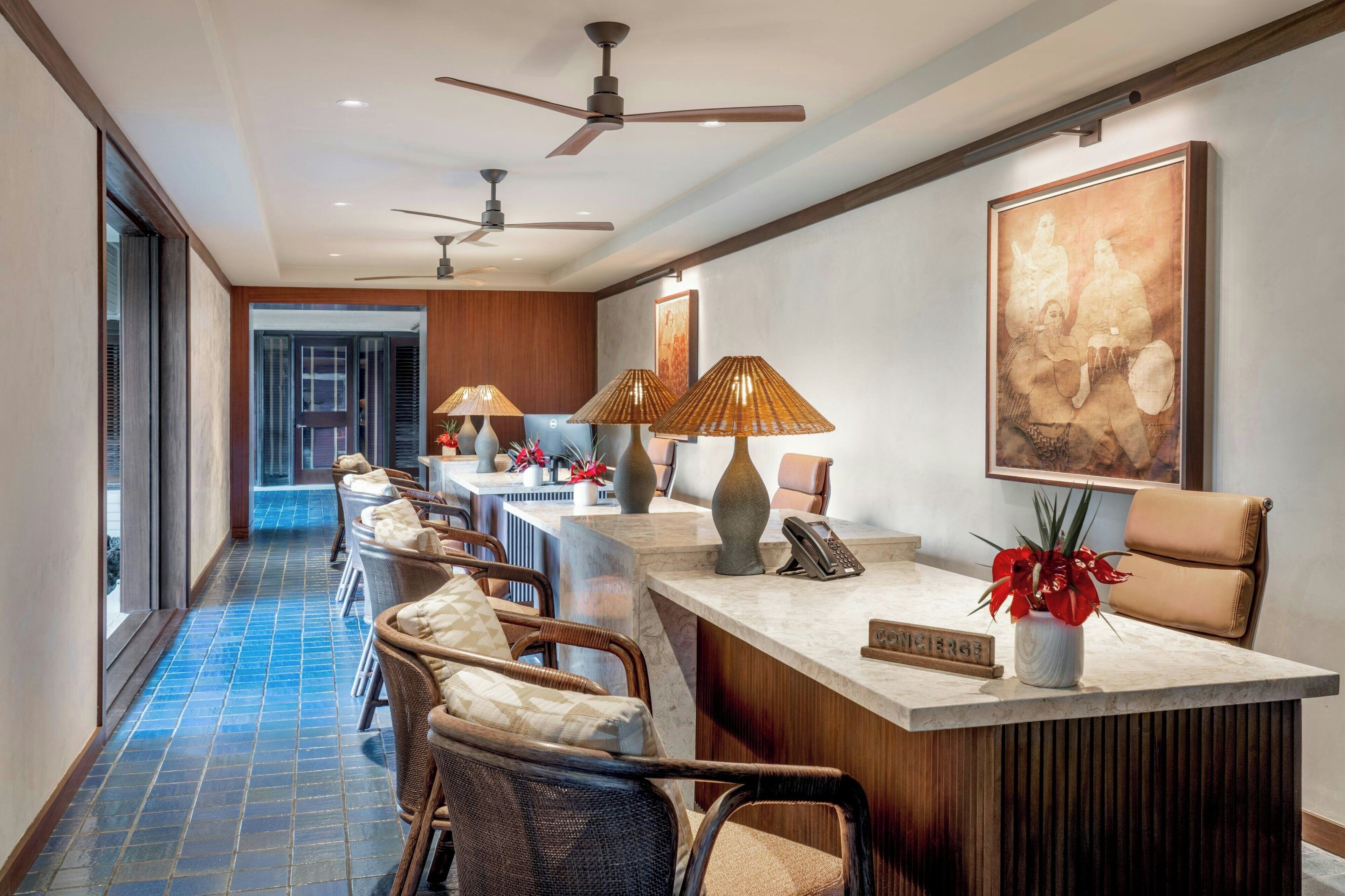 A reception area with a marble counter, wicker chairs, ceiling fans, and a large abstract painting on the wall.