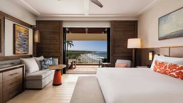 A hotel room with a bed, a sofa, a small table, a desk, a ceiling fan, a balcony with a view, and a painting on the wall.