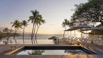 A poolside area with lounge chairs and umbrellas, overlooking a body of water and palm trees.