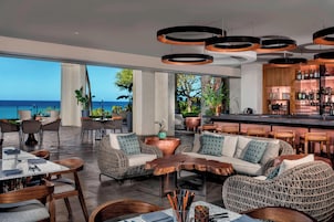 Uma área de bar moderna com móveis de vime, uma mesa de centro de madeira e vista para o oceano.