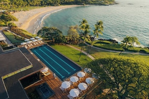 A pool area with lounge chairs and umbrellas, a beach, and palm trees.