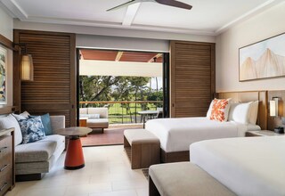 A hotel room with two beds, a sofa, a small table, and a balcony with a view of the outdoors.