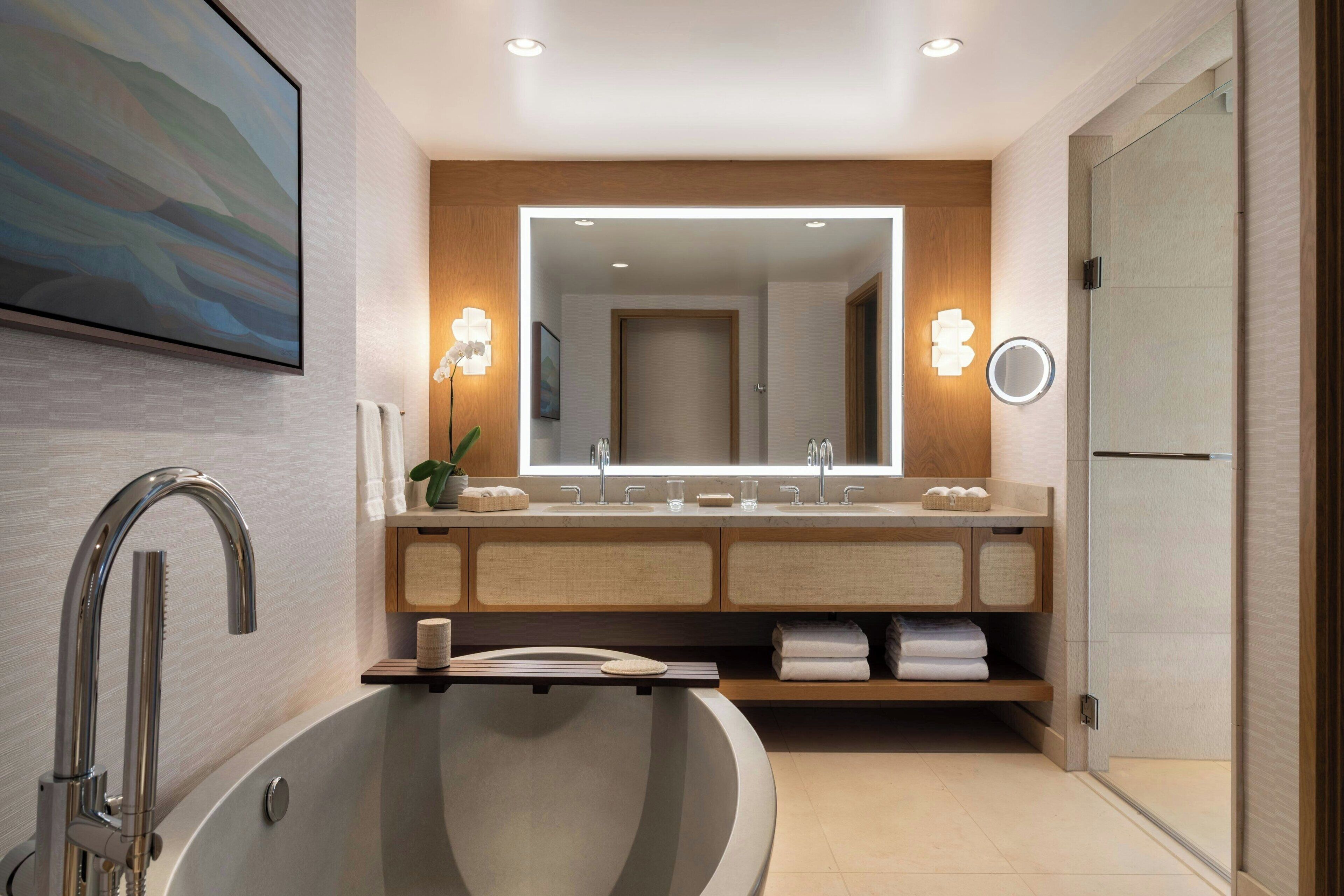 A modern bathroom with a freestanding bathtub, a large mirror, and a vanity with a sink and towel rack.