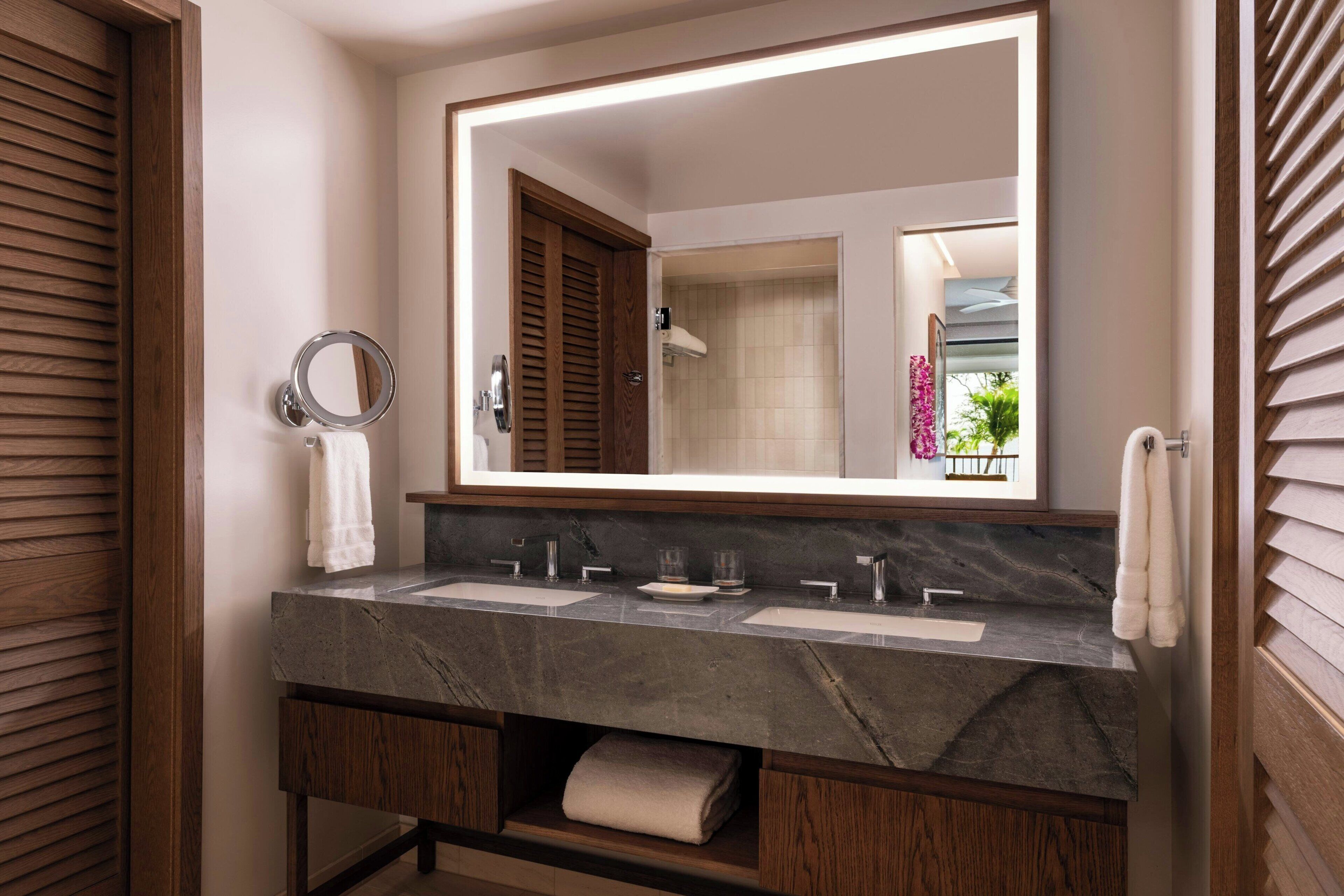 A bathroom with a large mirror, two sinks, and a towel rack.