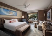 A modern hotel room with a large bed, a sofa, a dining table, and a balcony with a view of greenery.