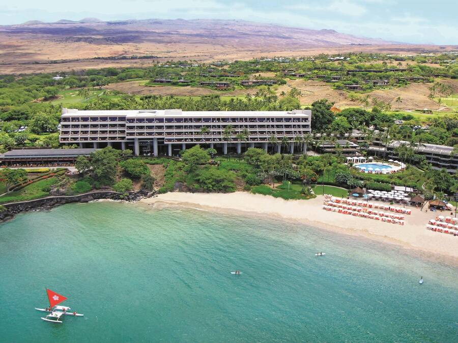A hotel with a large building, a beach, and clear turquoise water.