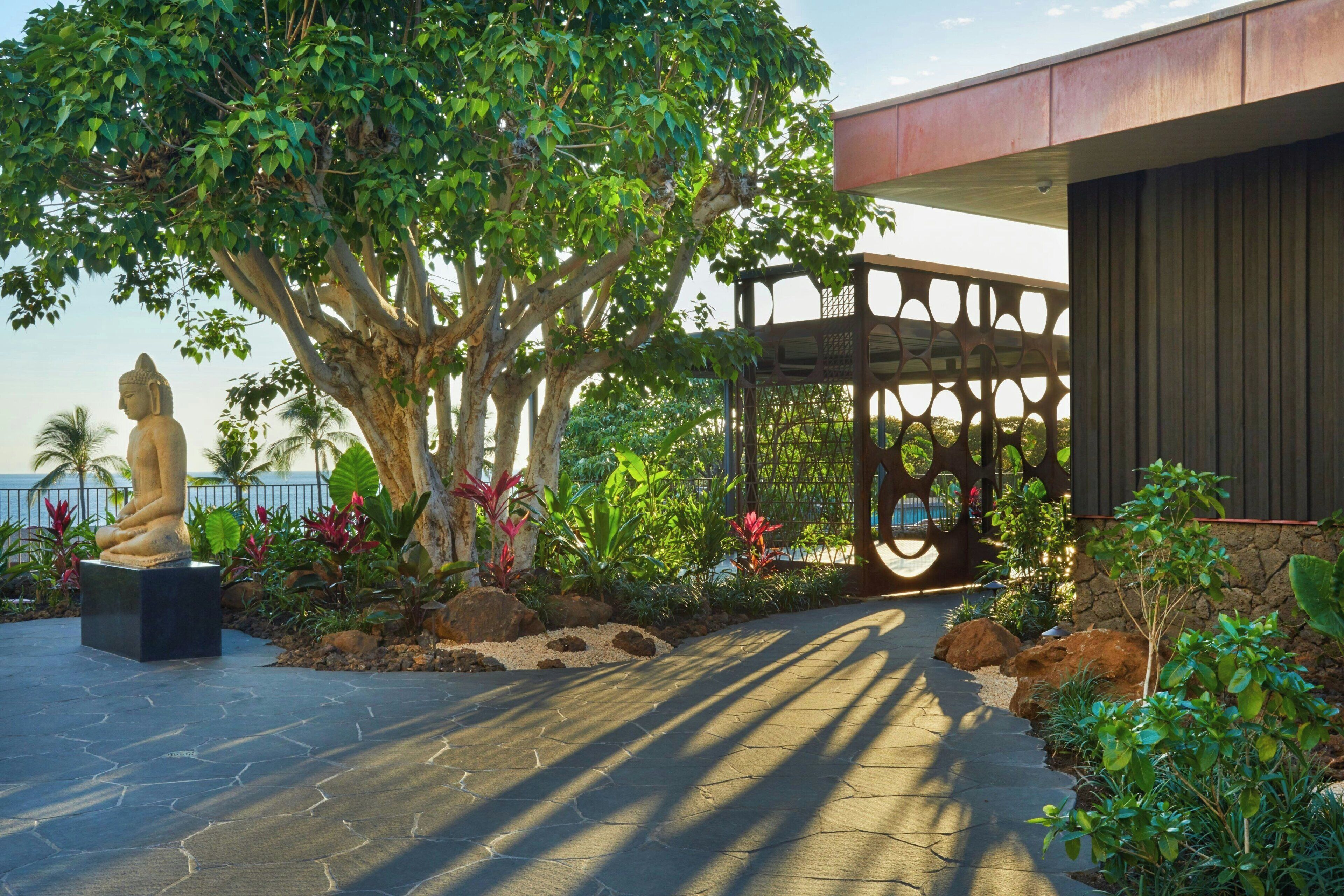 A garden with a statue, a tree, and a building with a wooden fence.