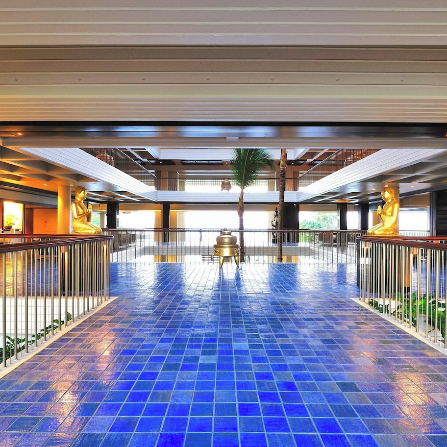 A spacious indoor area with a blue-tiled floor, metal railings, and a central statue.