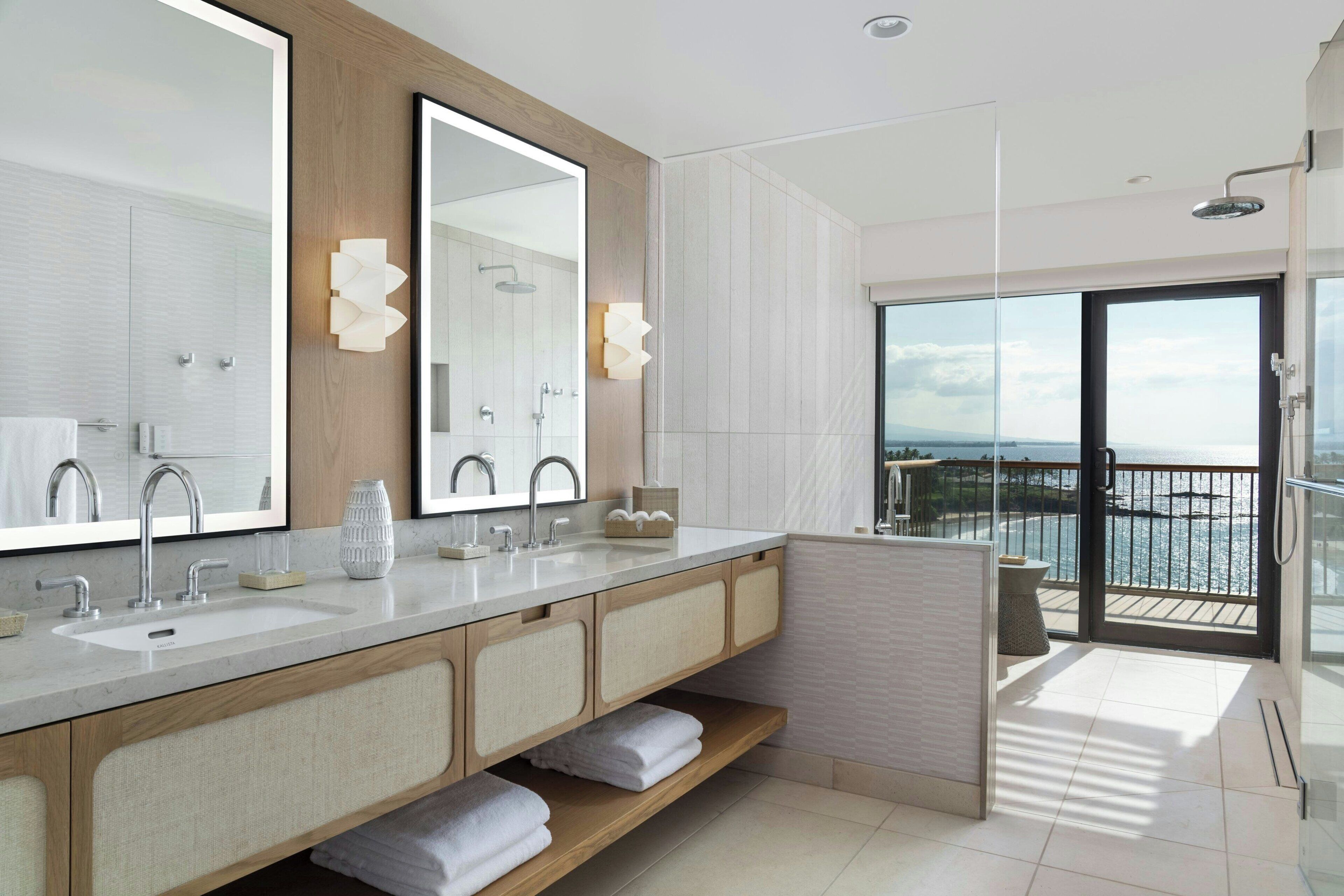 Un bagno moderno con uno specchio grande, due lavabi e una doccia. Dispone di un balcone con vista sul mare.