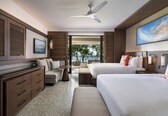 A hotel room with two beds, a sofa, a desk, and a view of the ocean.