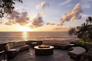A sunset view with a stone fire pit, a curved sofa, and a small table.