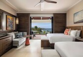 A hotel room with two beds, a sofa, a desk, a chair, a small table, and a balcony with a view.